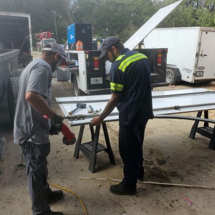 Two workers in safety gear inspect a metal frame at an outdoor worksite.