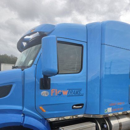 Blue FlowTrans semi-truck cab viewed from the side under a cloudy sky