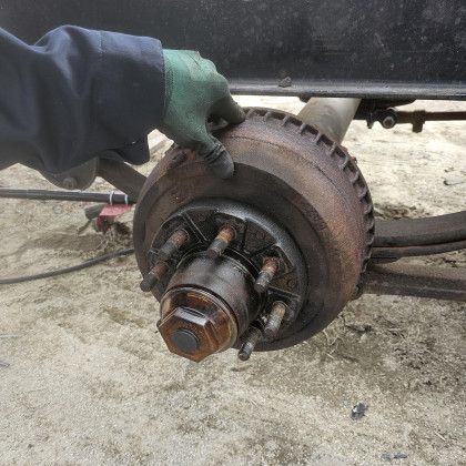 Gloved hand holding a rusty car brake rotor and hub assembly during repair