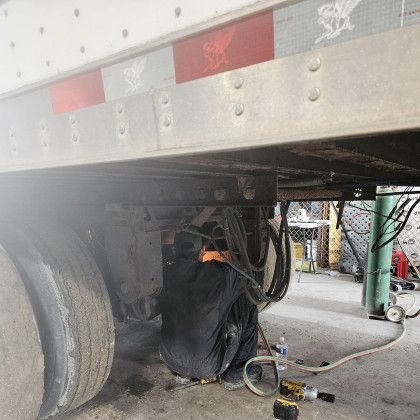 Large truck trailer with a damaged rear tire, hoses, and tools underneath in a garage or repair bay