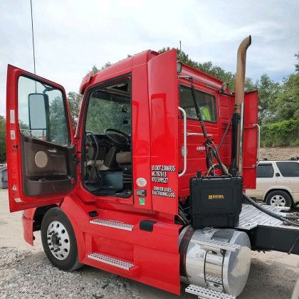 Red semi truck with open door and chrome fuel tank parked outdoors on gravel