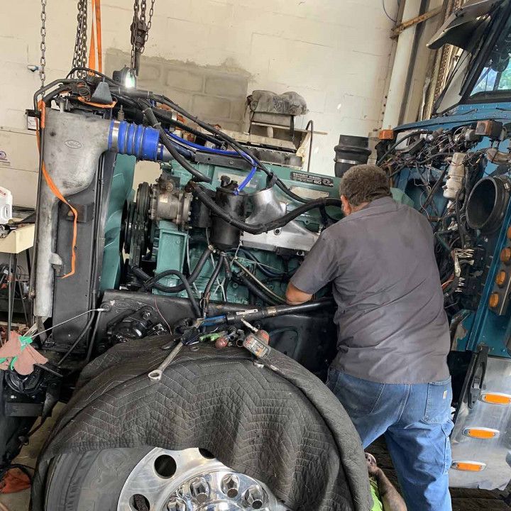 Mechanic working on a large engine in a garage, with hoses and machinery visible.