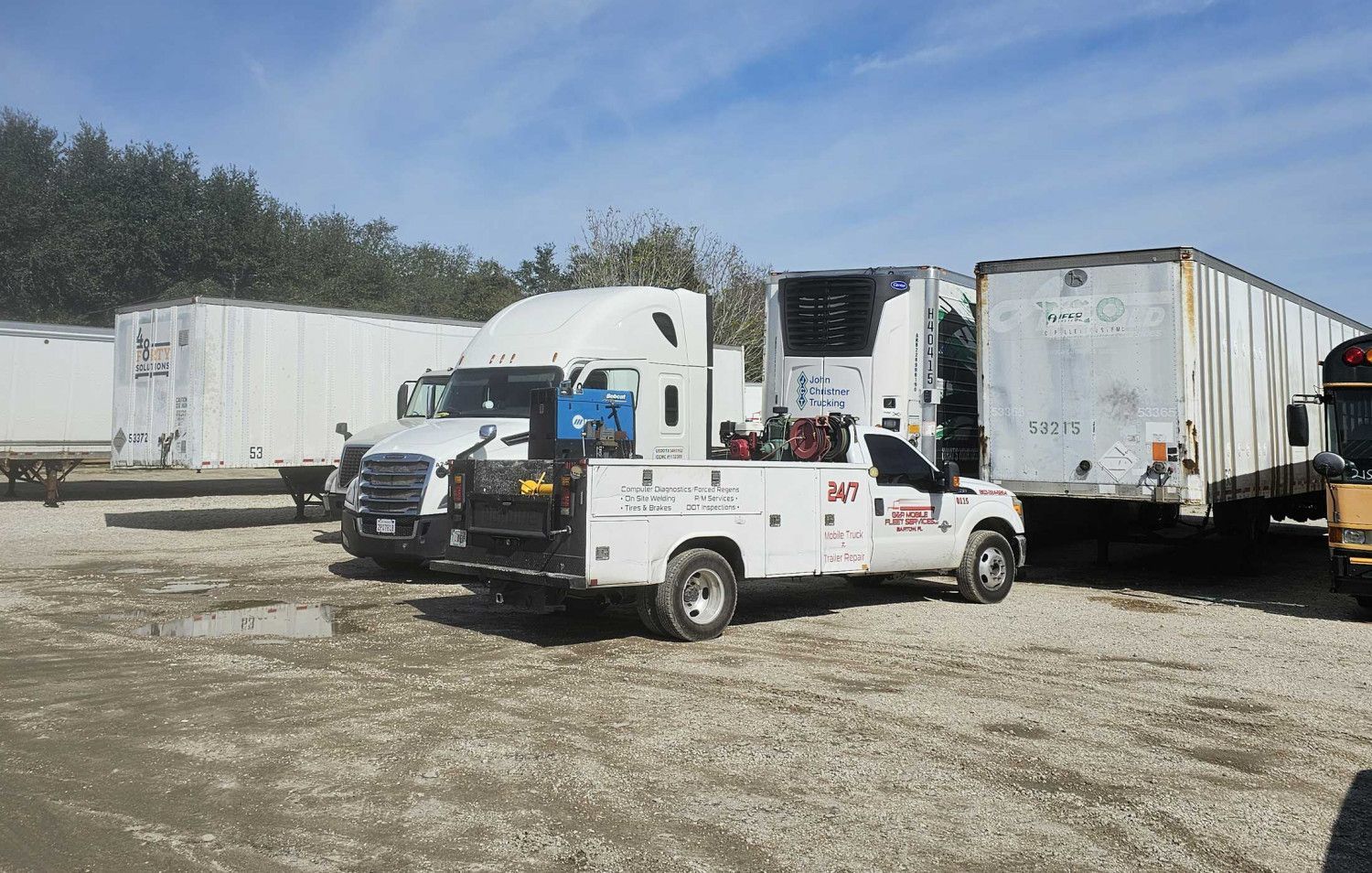 White truck and several trailers parked on a gravel lot in daylight