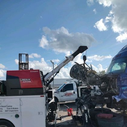 Tow truck lifting a wrecked car at a roadside salvage yard under a blue sky