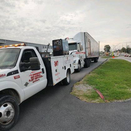 White tow truck towing a white box truck along a roadside at dusk