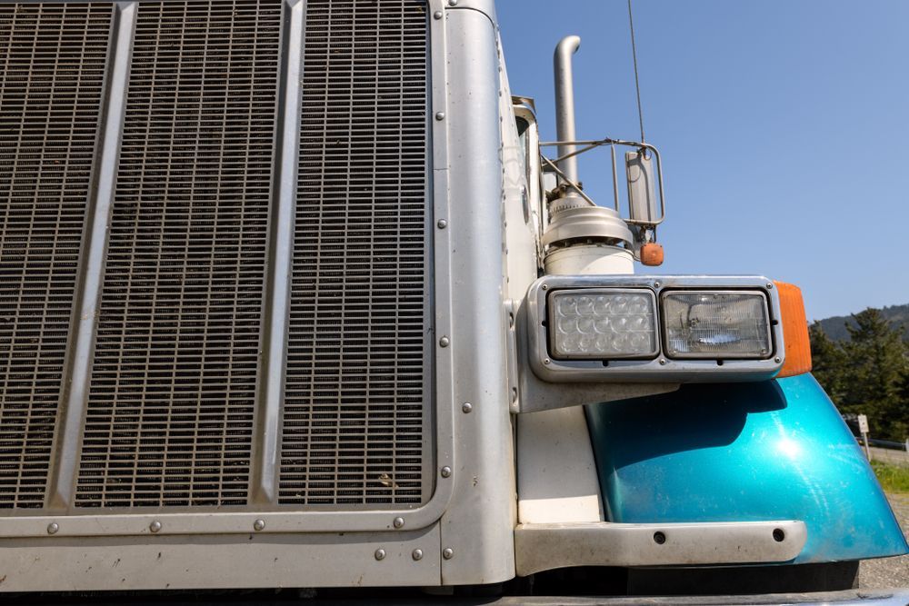 Close-up of a semi-truck front with chrome grille, headlights, and a blue hood under a clear sky