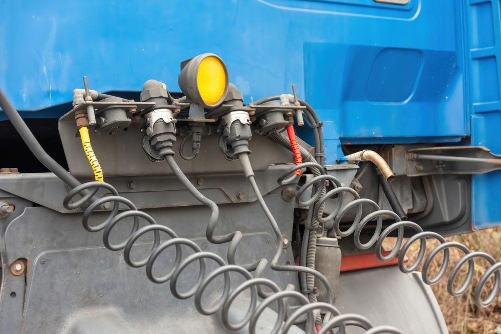 Blue truck rear with coiled air hoses and yellow connector on a gray utility panel