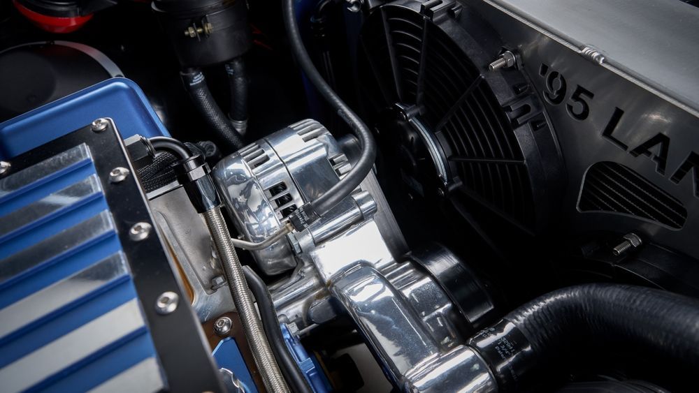 Close-up of a chrome engine with blue-striped cover and black fan in a car engine bay