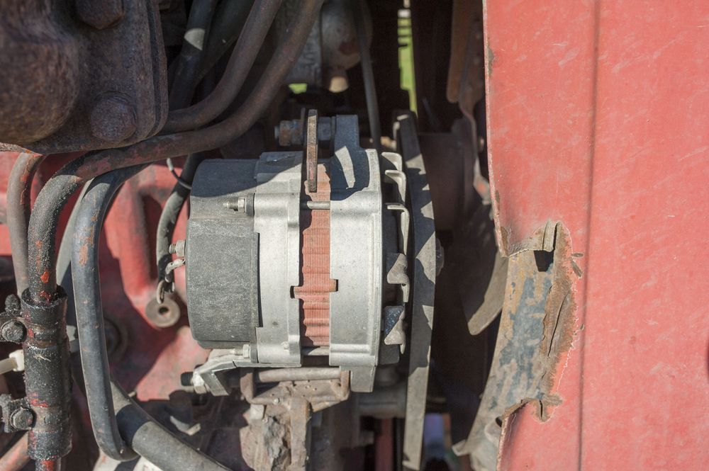 Close-up of a car alternator and wiring inside an engine compartment, with rusted metal nearby.