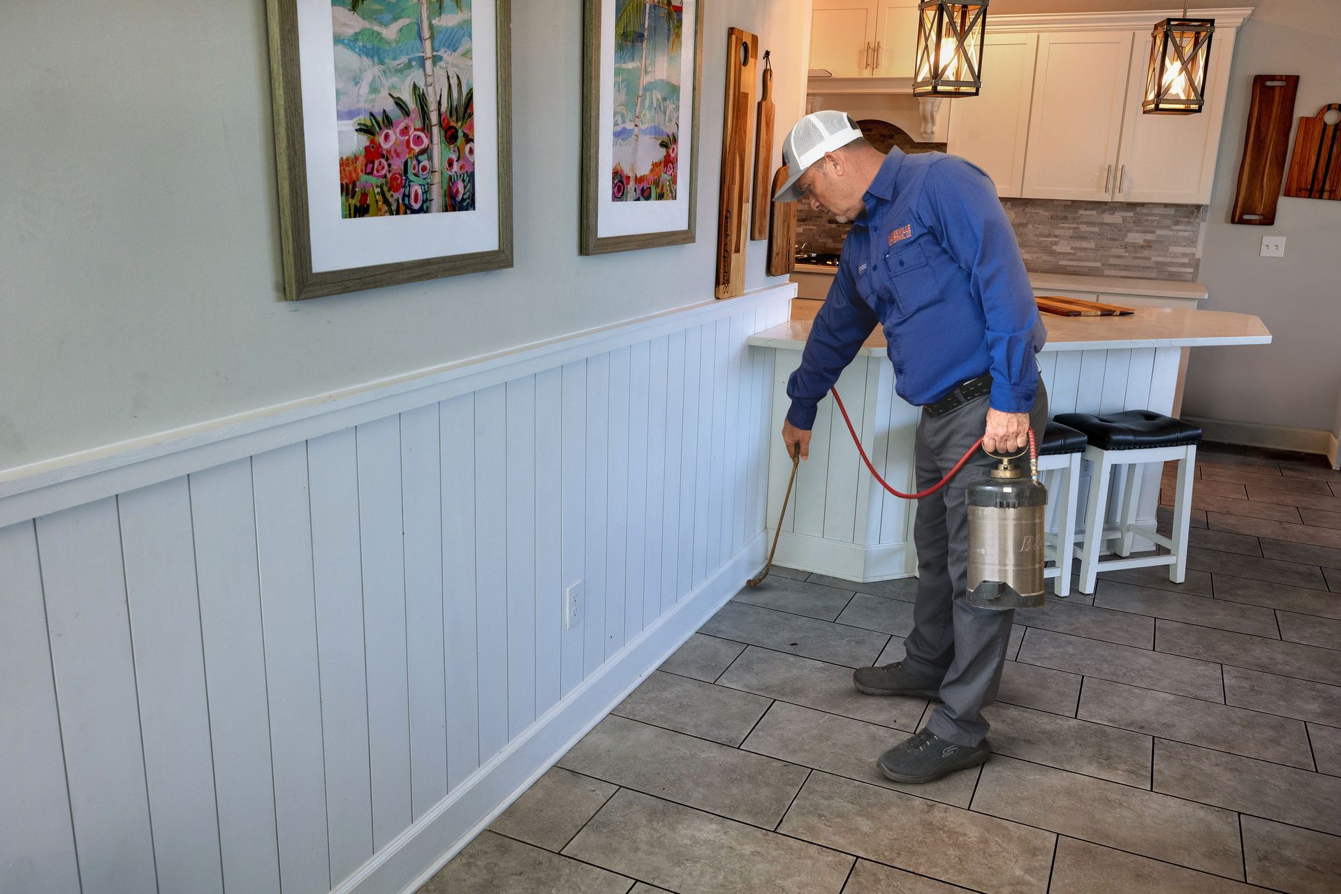 Pest control technician applying treatment along a baseboard inside a residential kitchen. Pest control technician applying treatment along a baseboard inside a residential kitchen.