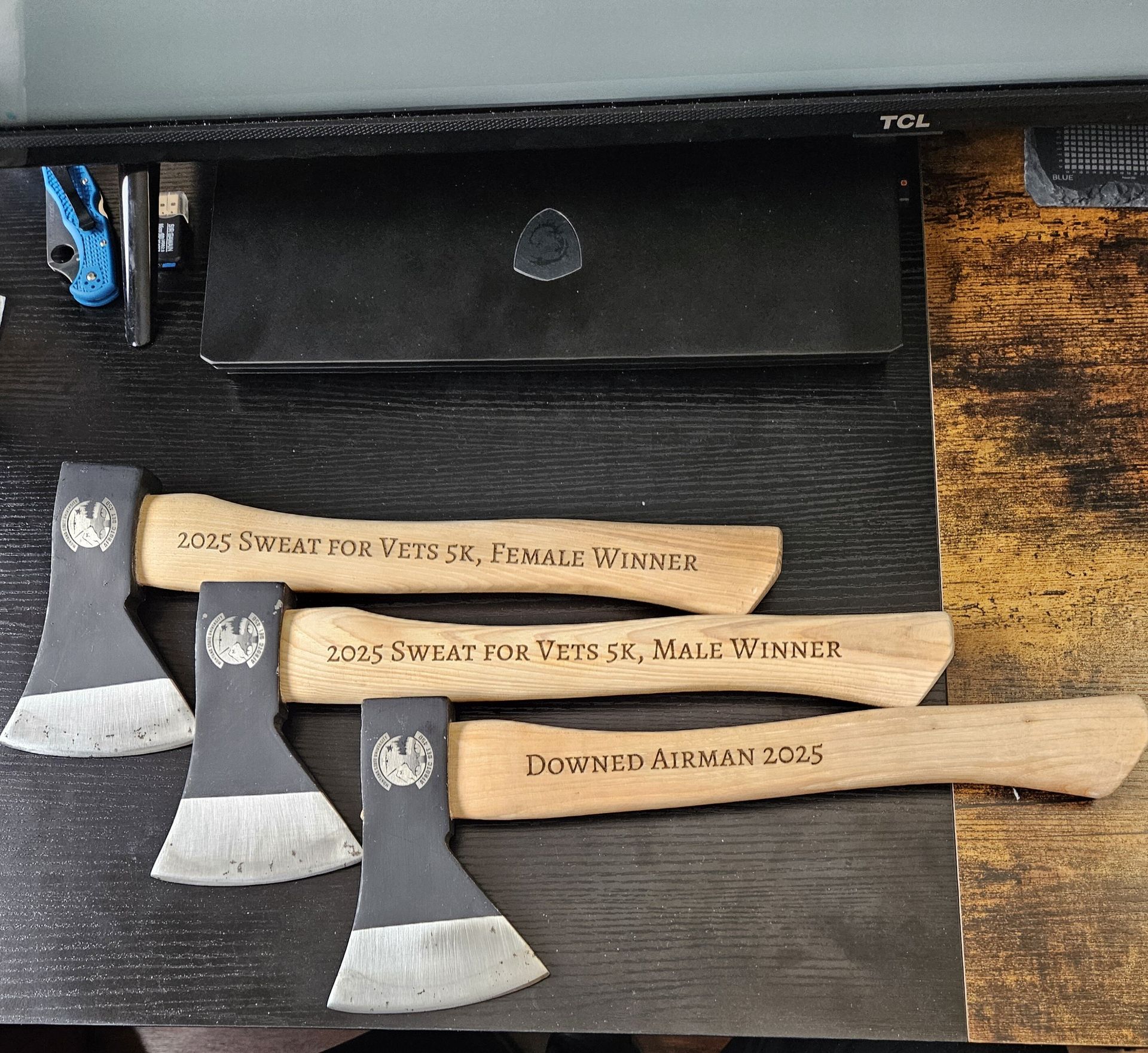 Three engraved hatchets on a black mat, displayed in front of a black box.