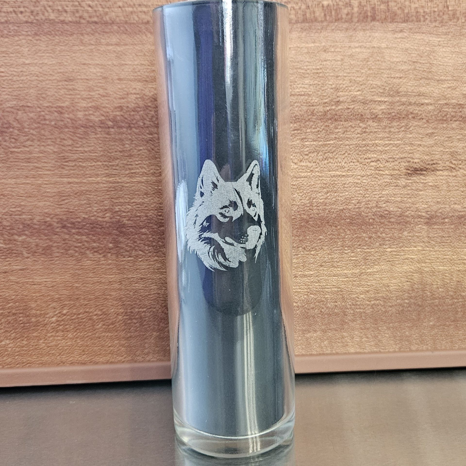 Close-up of a silver folding knife blade with a spider logo on a dark wooden surface