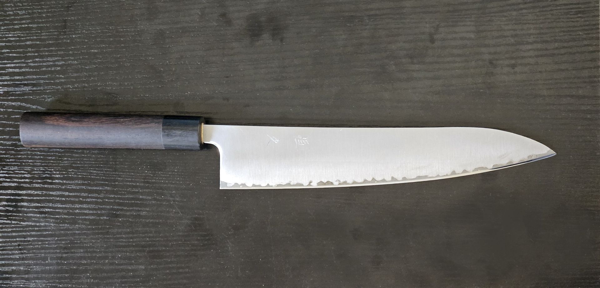 Kitchen knife with black handle and blue accent lying on a dark wood surface.