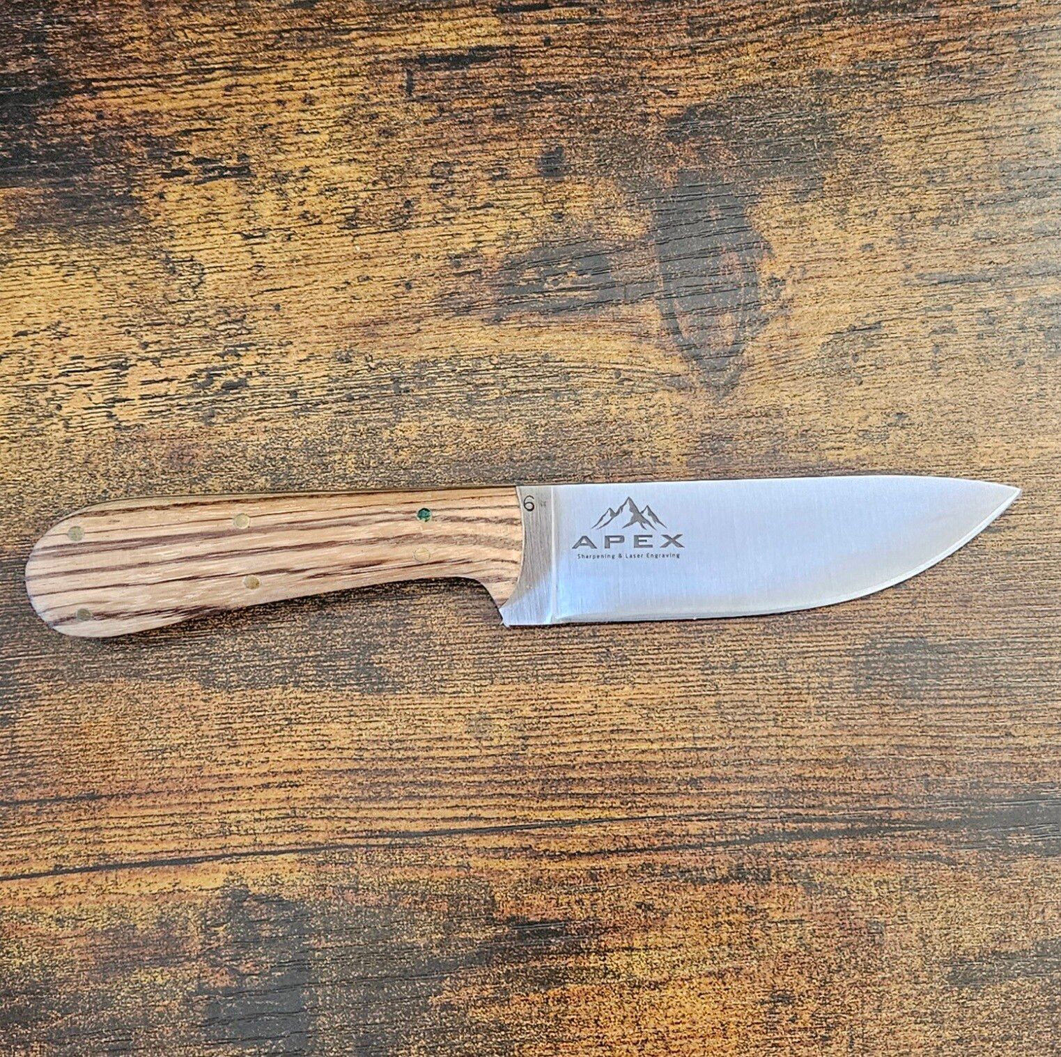 Small fixed-blade knife with a wooden handle on a weathered wooden surface.