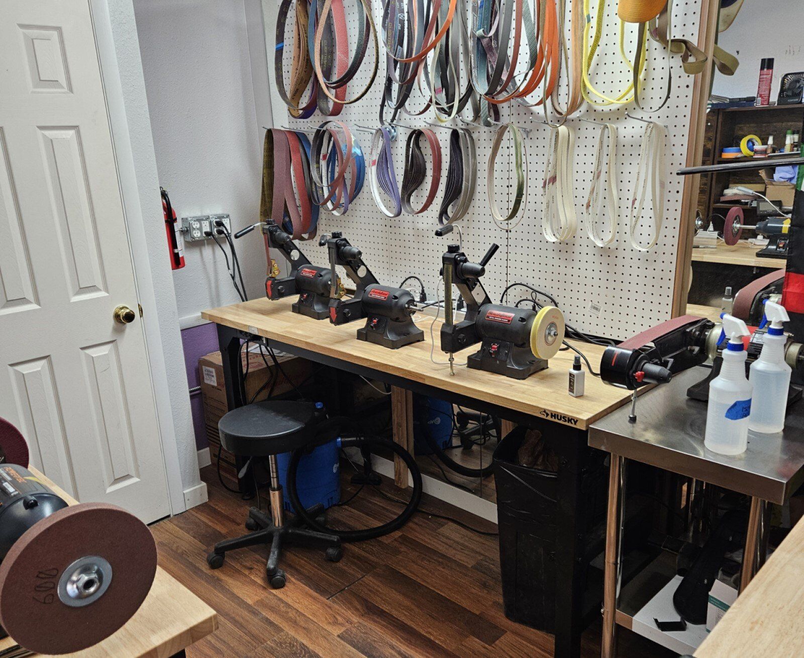 A workshop bench with tools, hanging straps, stools, and a pegboard in a small room.