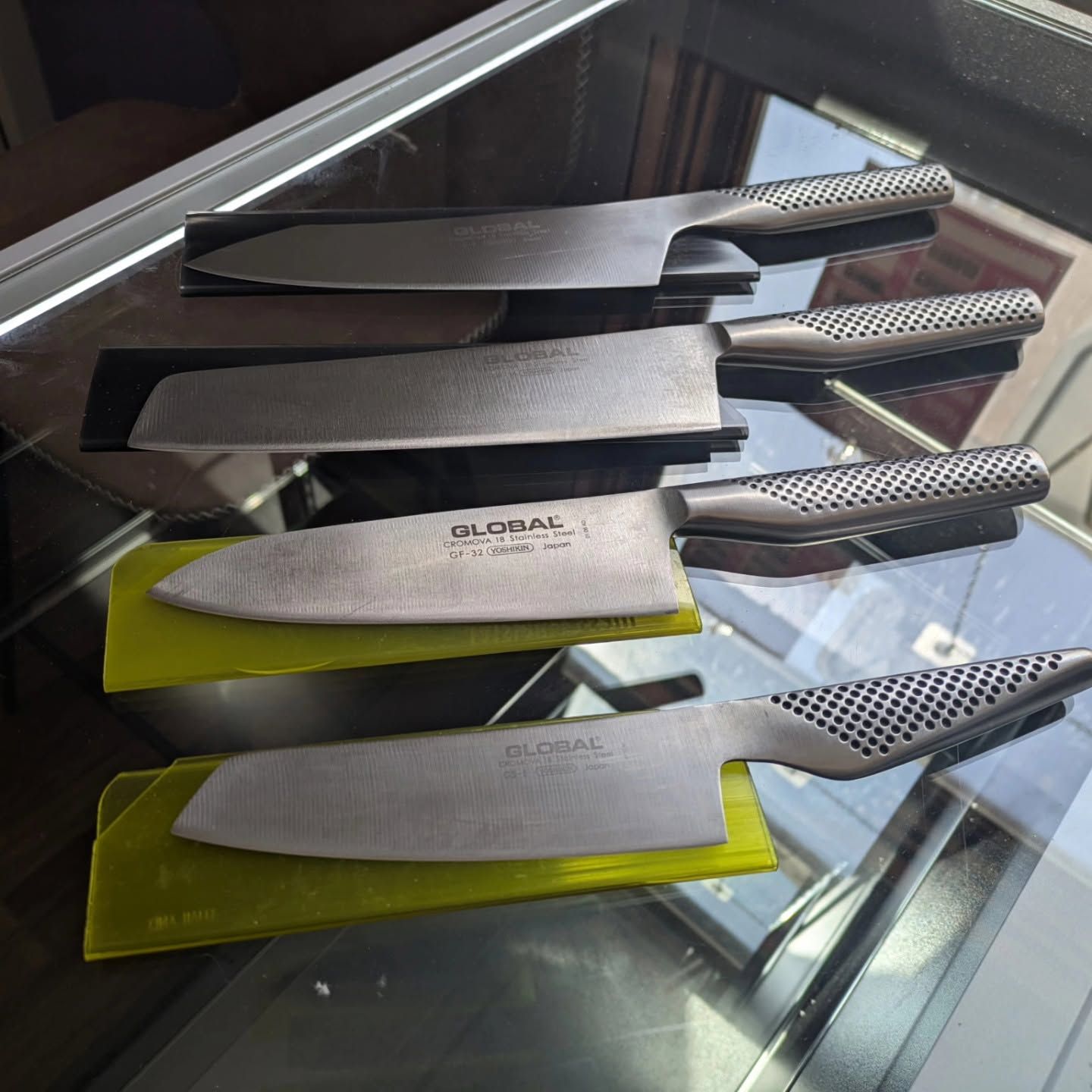 Four kitchen knives on a glass surface, with black and yellow handles and blades visible.