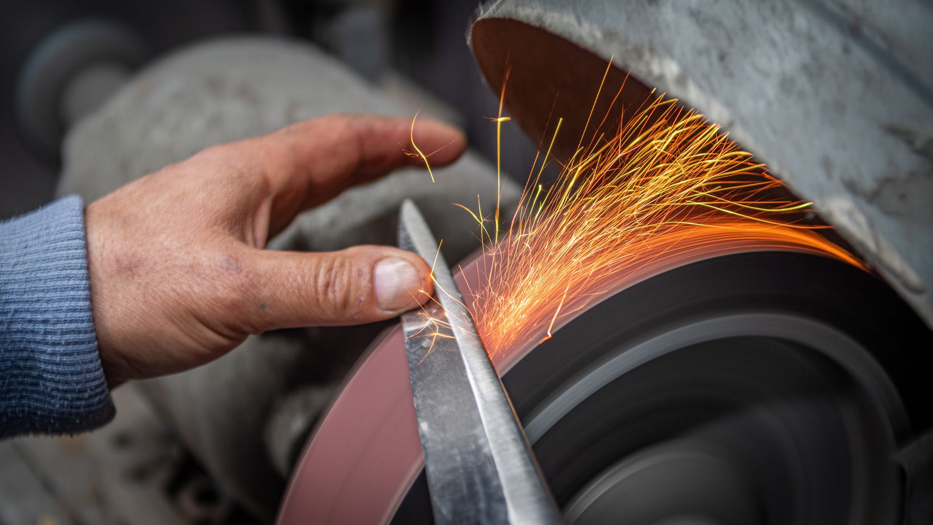 Hands grinding metal on a wheel, with bright sparks flying.