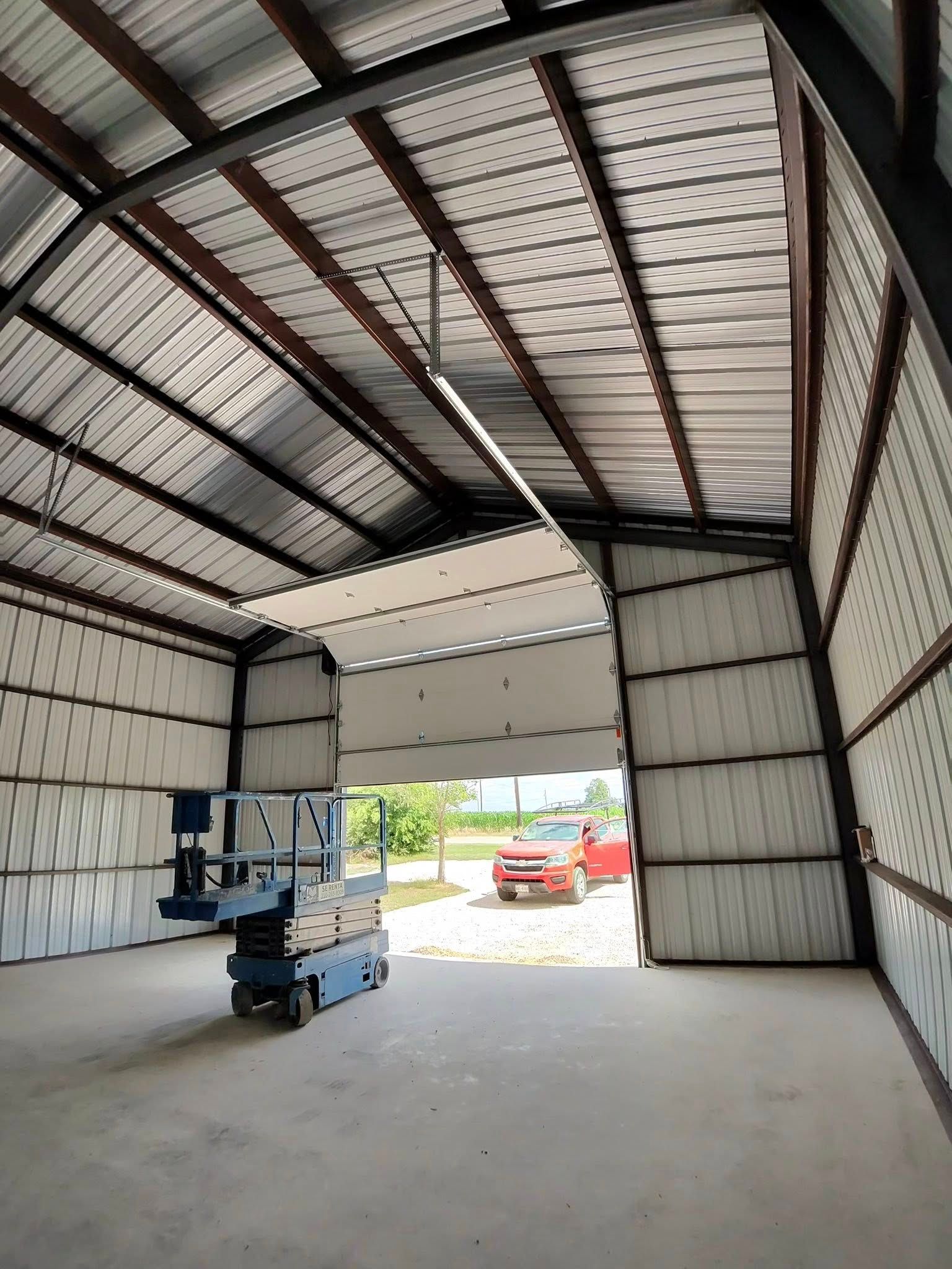 Empty metal workshop with open garage door and a small lift, red car visible outside.