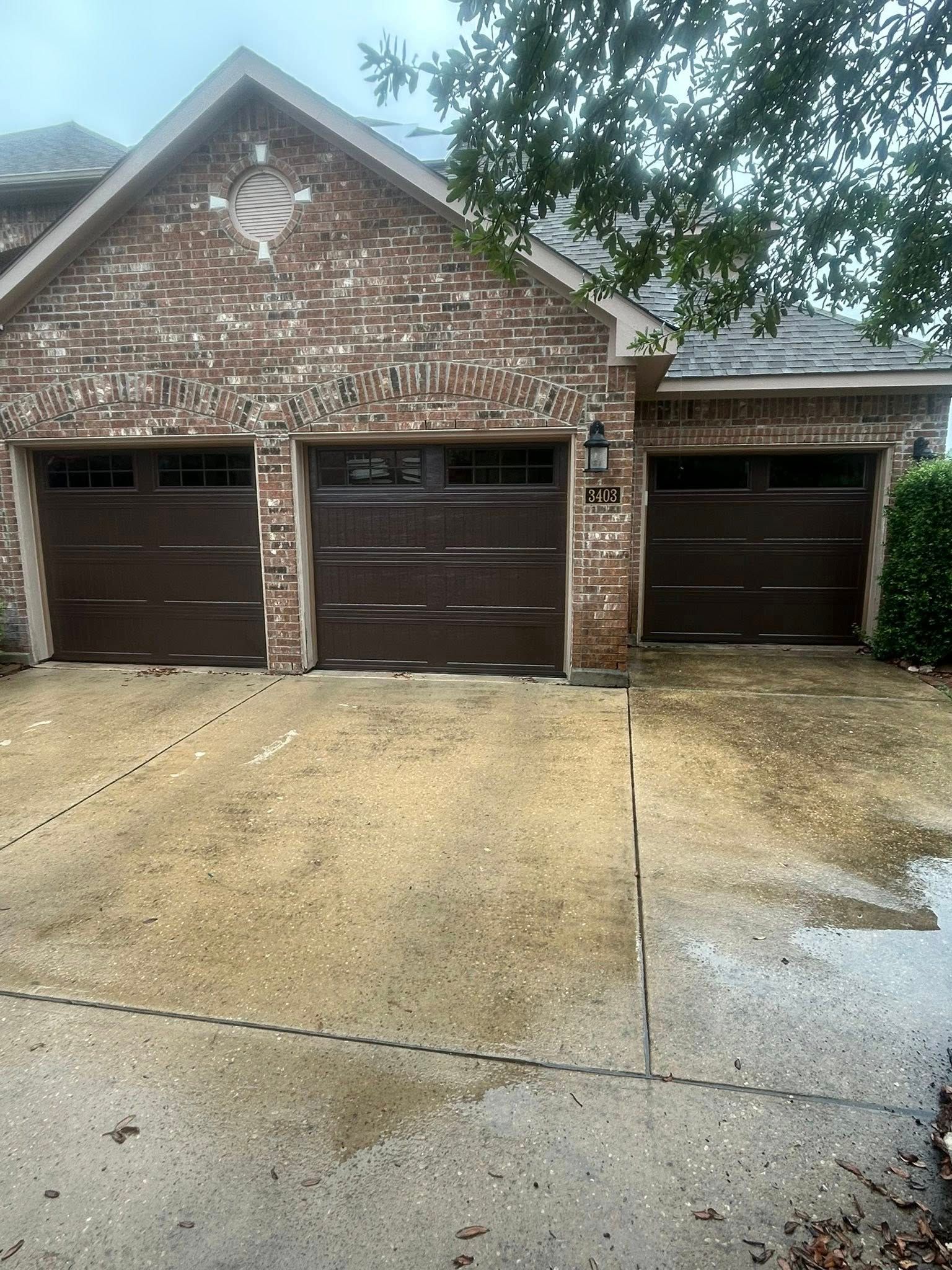 Brick house with three garage doors and a wet driveway under a cloudy sky