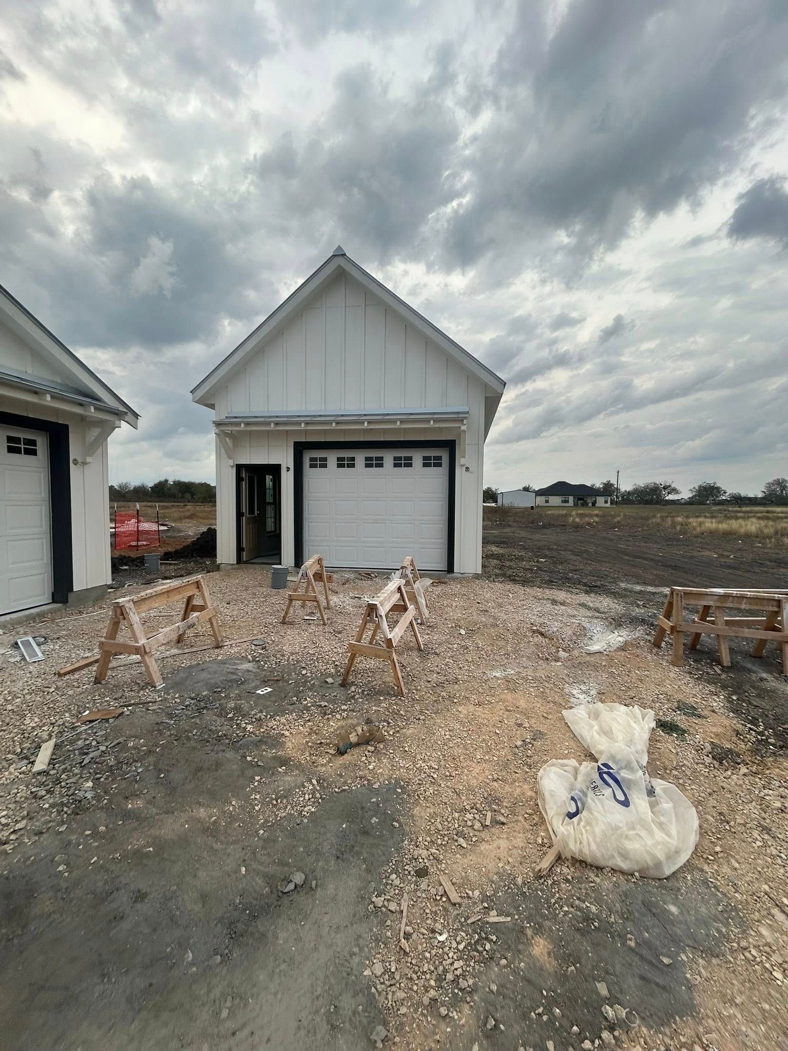 Small white garage under construction beside a muddy gravel lot beneath cloudy skies
