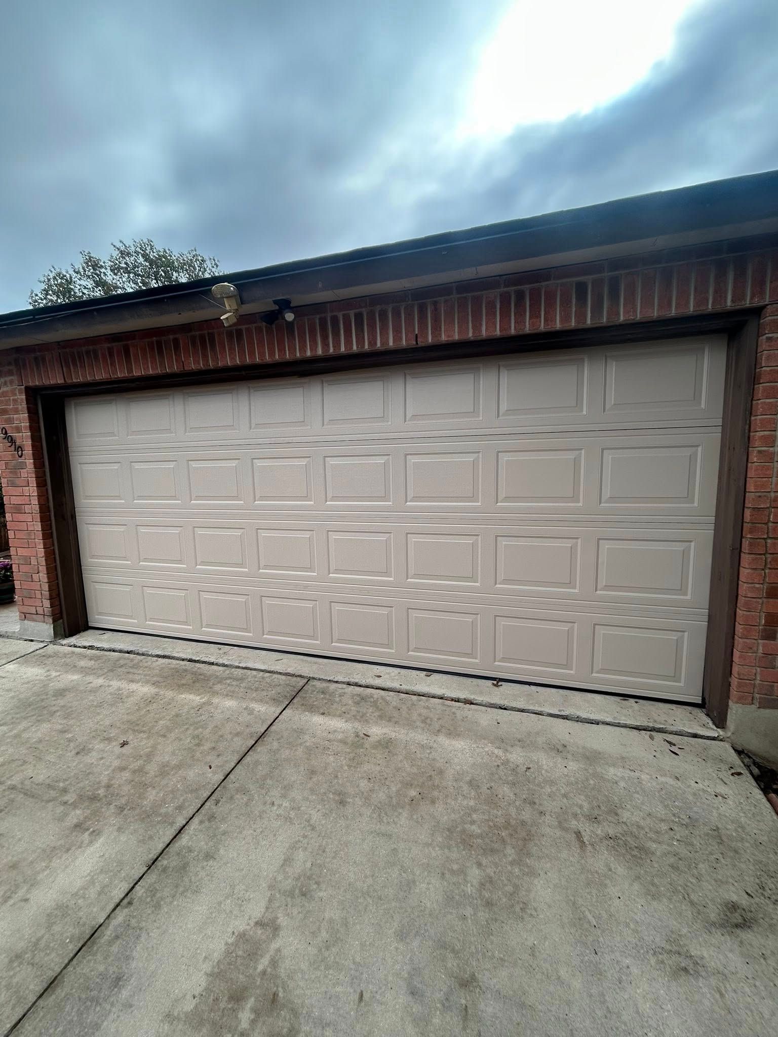 Residential garage door with beige panels in a brick driveway under a cloudy sky
