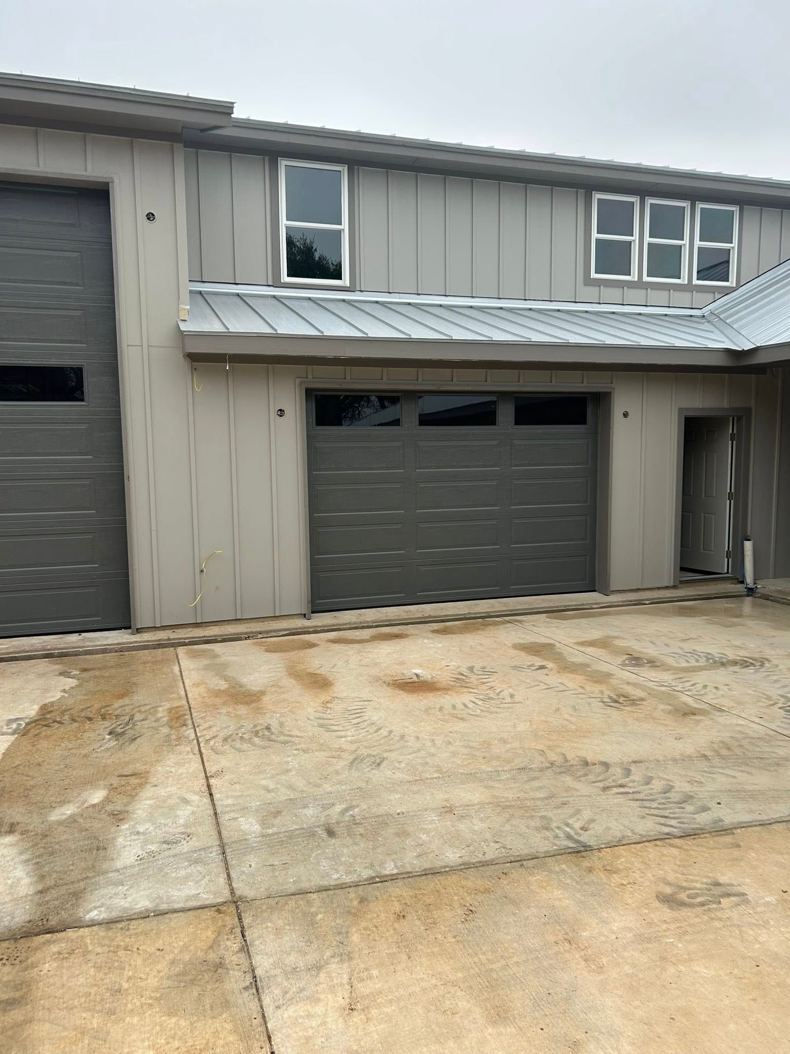 Two-story gray townhouse with garage and weathered concrete driveway under cloudy sky