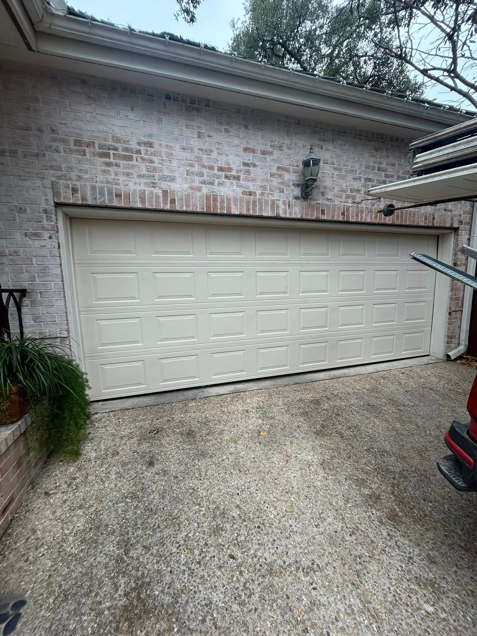 White double garage door on a brick house with gravel driveway and a potted plant nearby