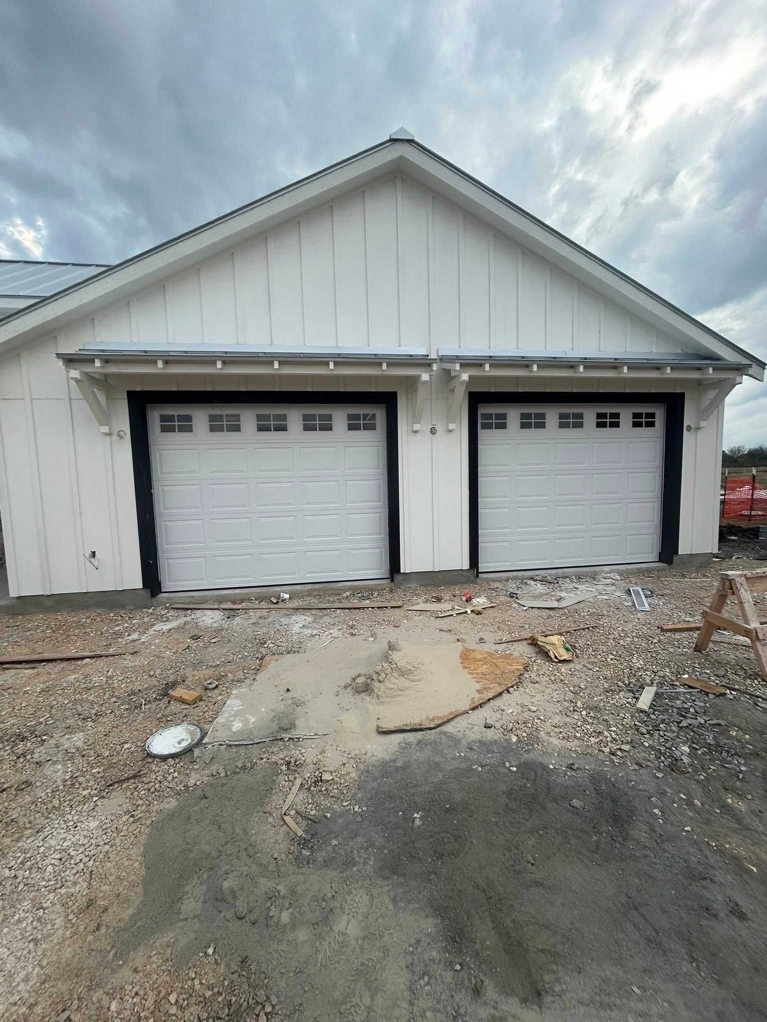 White detached garage with two white doors on a gravel driveway under a cloudy sky