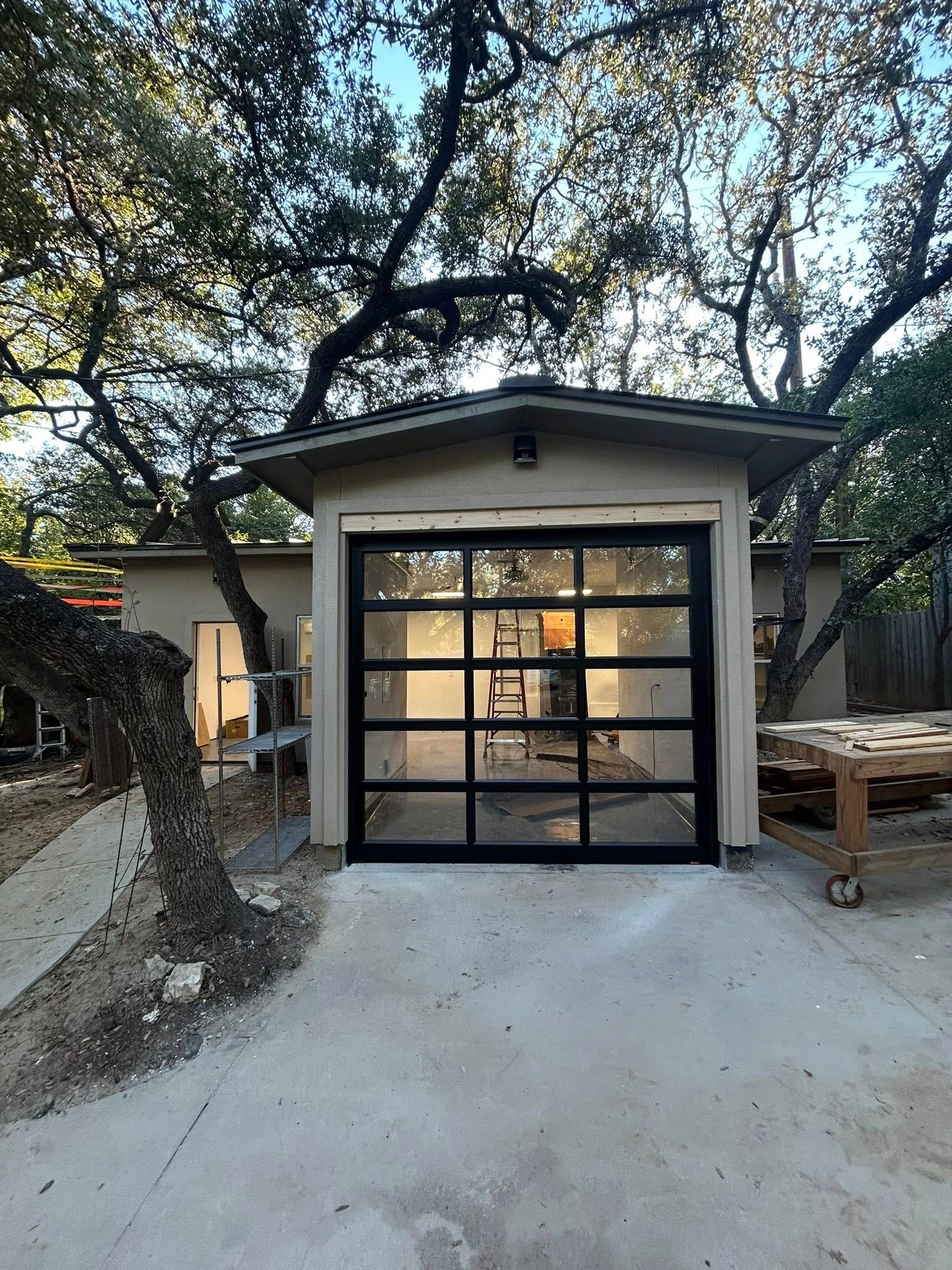 Small modern garage with glass door under trees, set in a concrete driveway.
