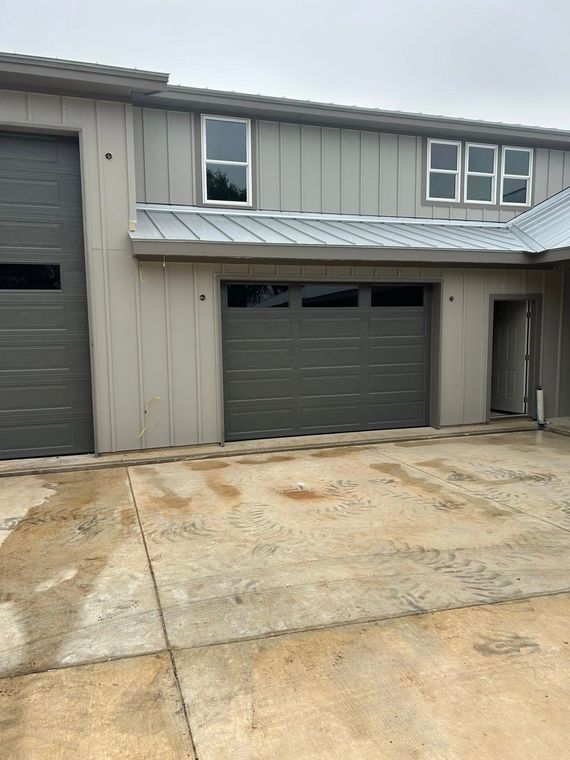 Gray townhouse exterior with garage doors and a concrete driveway.