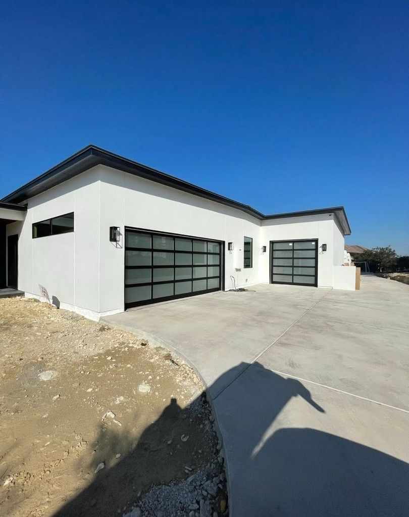 Modern white house under construction with black garage doors and a concrete driveway under a clear blue sky