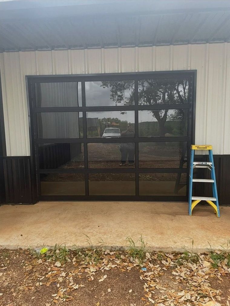 Front porch with dark glass doors, black lower siding, and a yellow step ladder on the right.