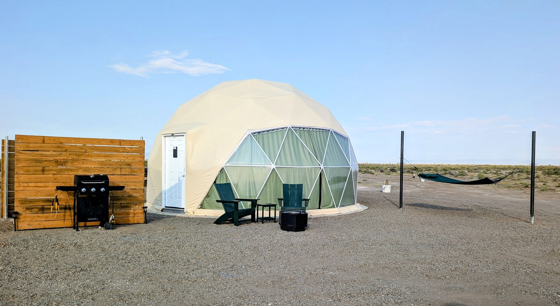 Dome tent and small wood shed on a rocky beach under a clear blue sky