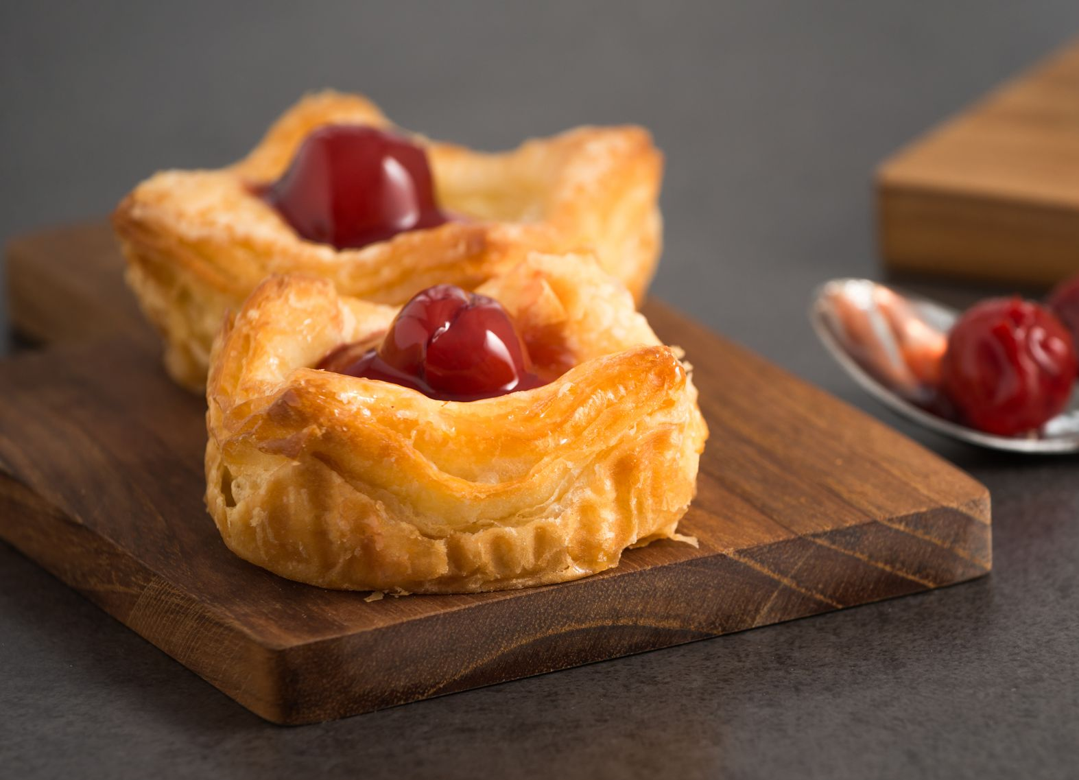 Two cherry pastries on a wooden board, with a spoon and cherries beside them