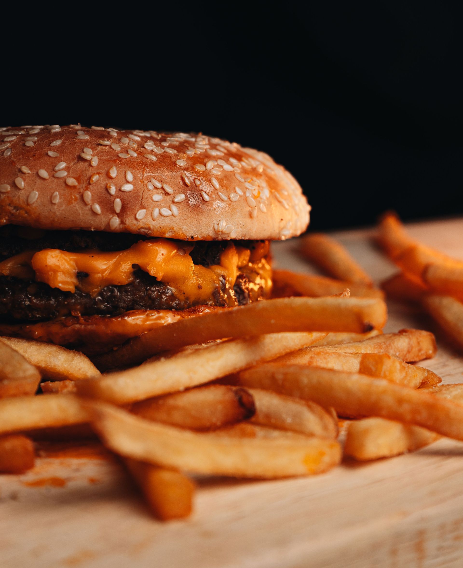 Sesame burger with melted cheese and fries on a wooden board