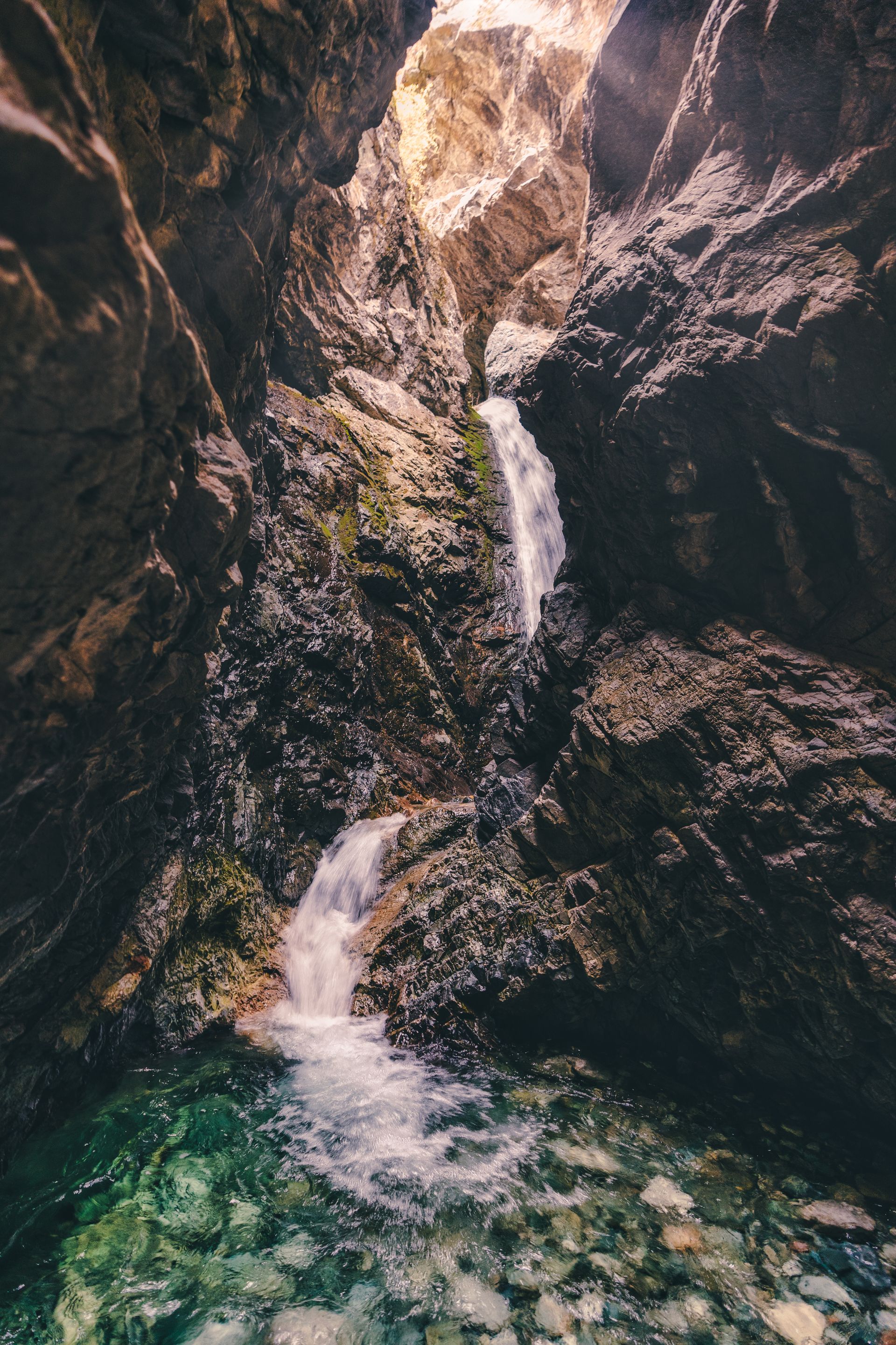 Narrow waterfall cascading through a rocky canyon into a clear pool