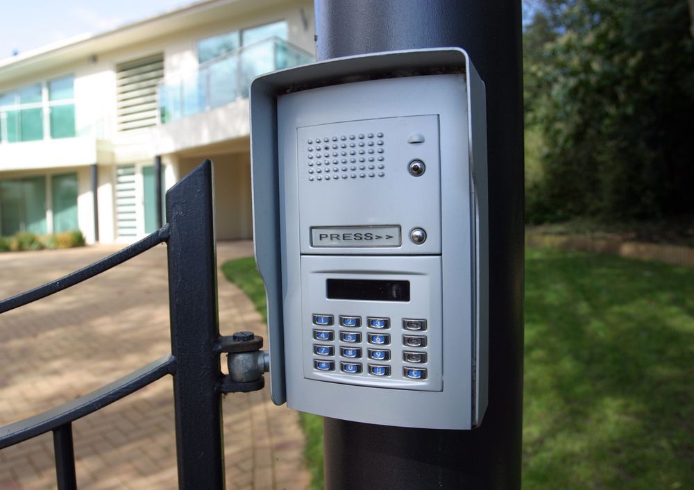 Intercom System With Keypad Mounted on a Black Post Near a Gate and Modern House — Gate-O-Matic in Garbutt, QLD
