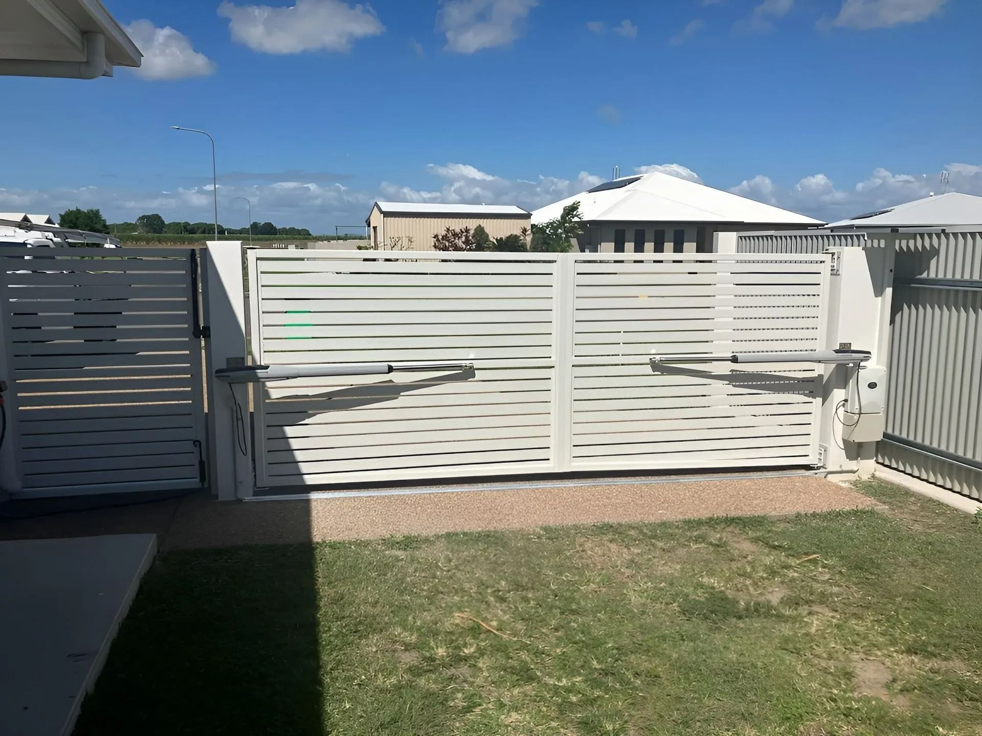 White Slatted Driveway Gate, Open, in Front of a House on a Sunny Day — Gate-O-Matic in Garbutt, QLD