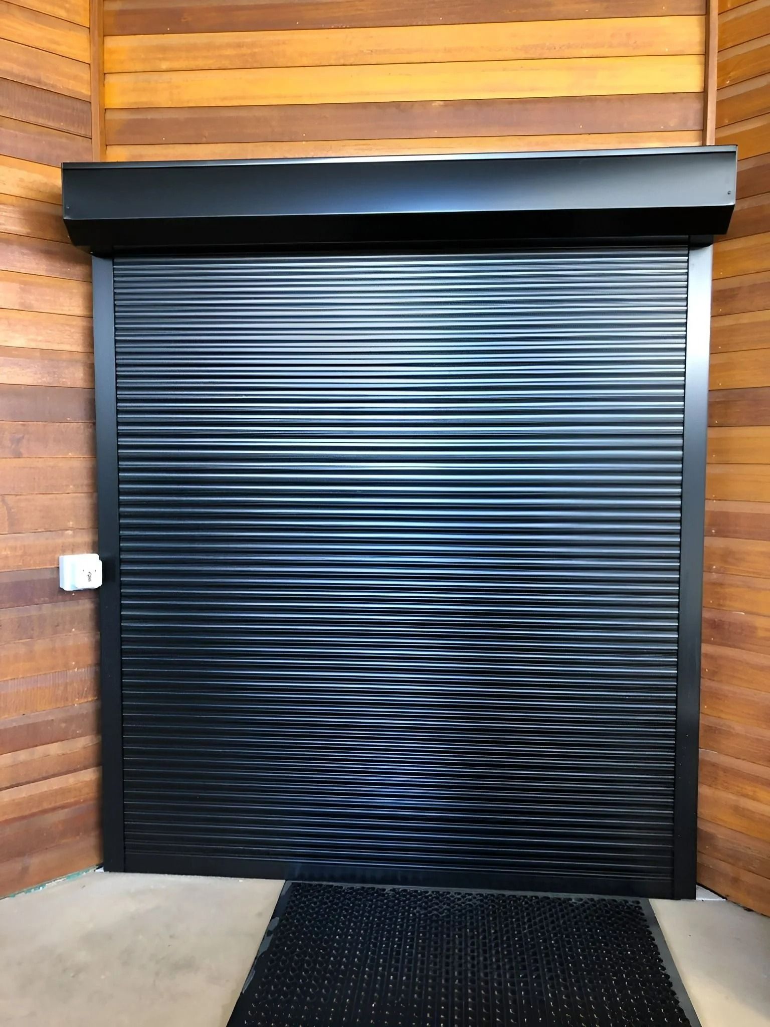 A Closed Black Roller Shutter Door Installed on a Curved Wooden Wall — Gate-O-Matic in Garbutt, QLD