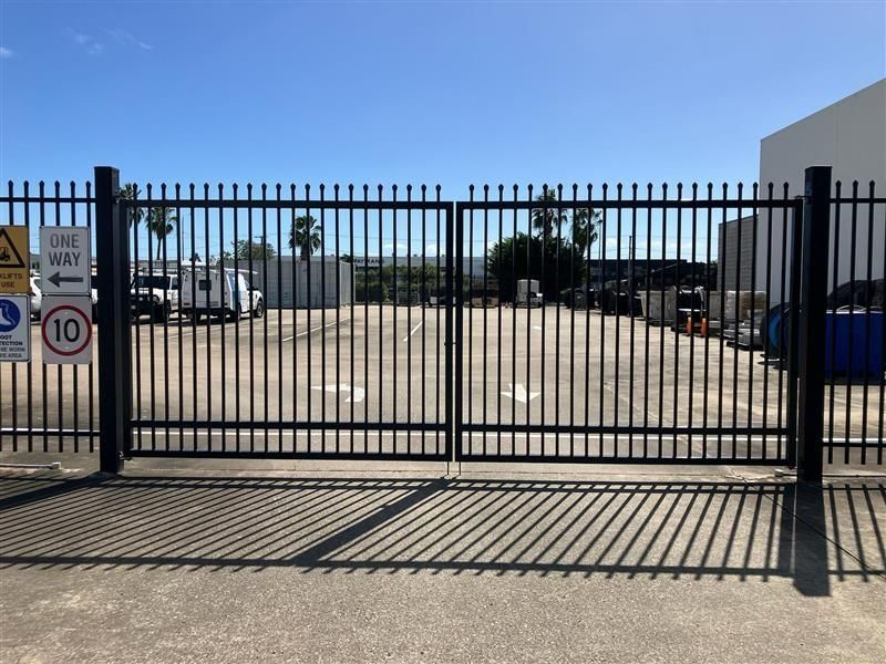 Black Metal Gate, Closed, in Front of a Concrete Area With Industrial Buildings and Blue Sky — Gate-O-Matic in Garbutt, QLD