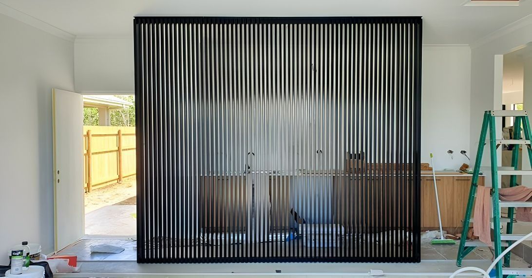 Black vertical slat room divider, partially obscuring a kitchen. Open door leads to a backyard — Gate-O-Matic in Garbutt, QLD