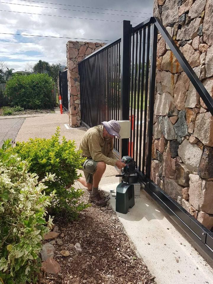Man Kneeling, Working on Gate Opener, Next to Black Gate and Stone Wall — Gate-O-Matic in Garbutt, QLD