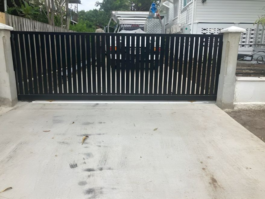 Black Metal Gate With Vertical Bars on a Concrete Driveway — Gate-O-Matic in Garbutt, QLD