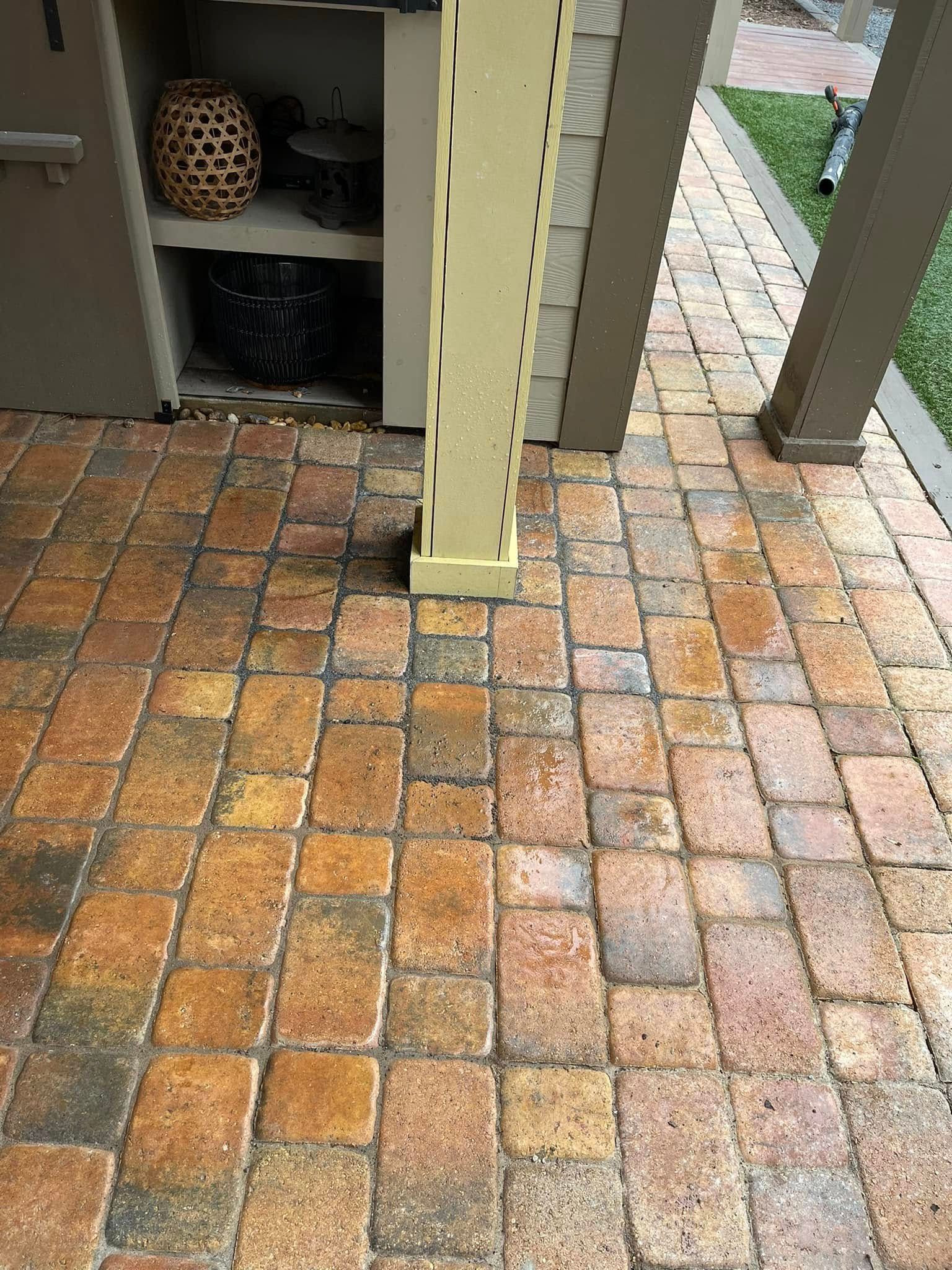 A textured brick patio surface featuring earthy tones of brown and tan, with a vertical support post in the foreground.