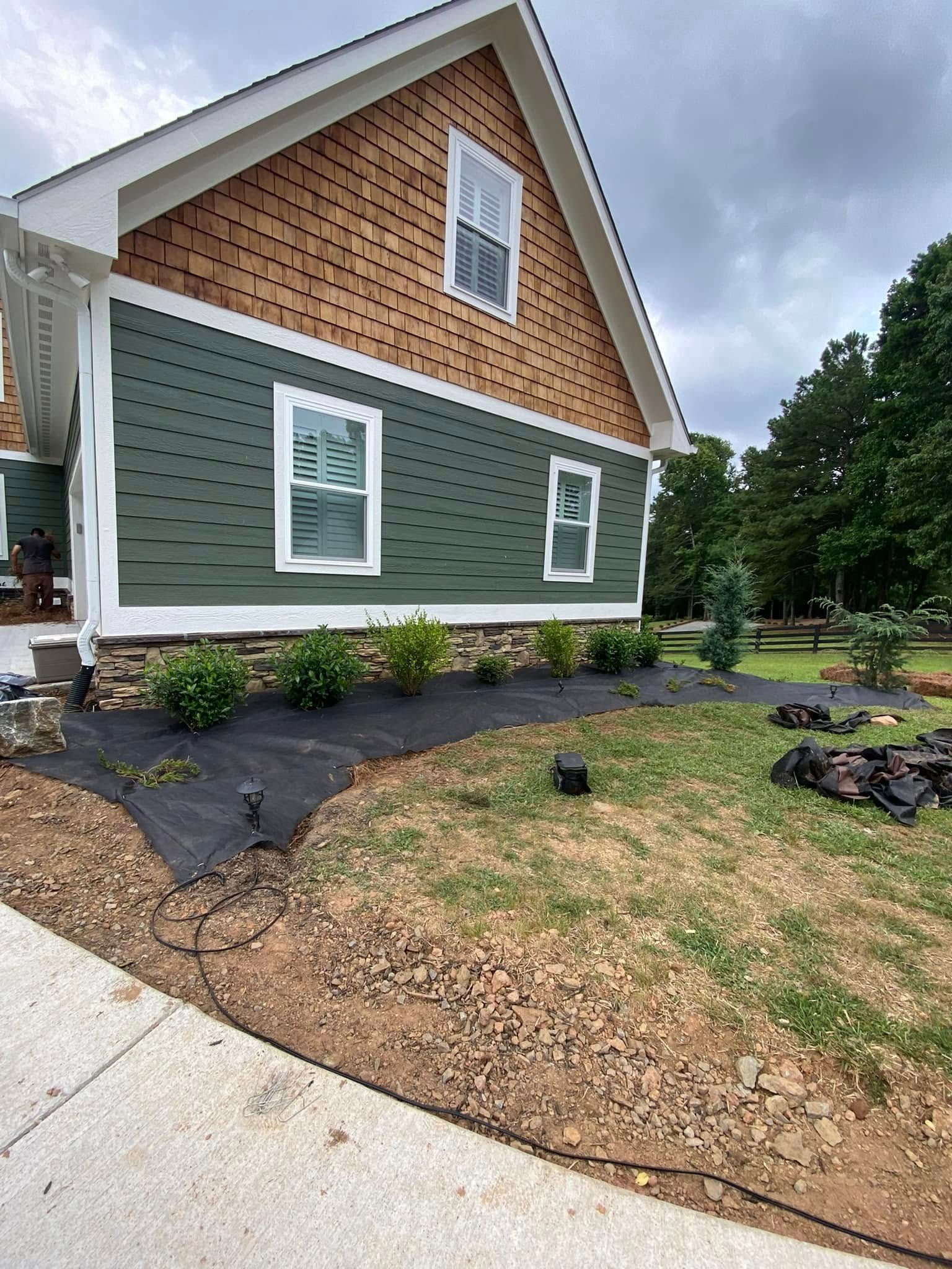 A house exterior with green horizontal siding, brown wood shingles in the gable, and a landscaped bed with new mulch.