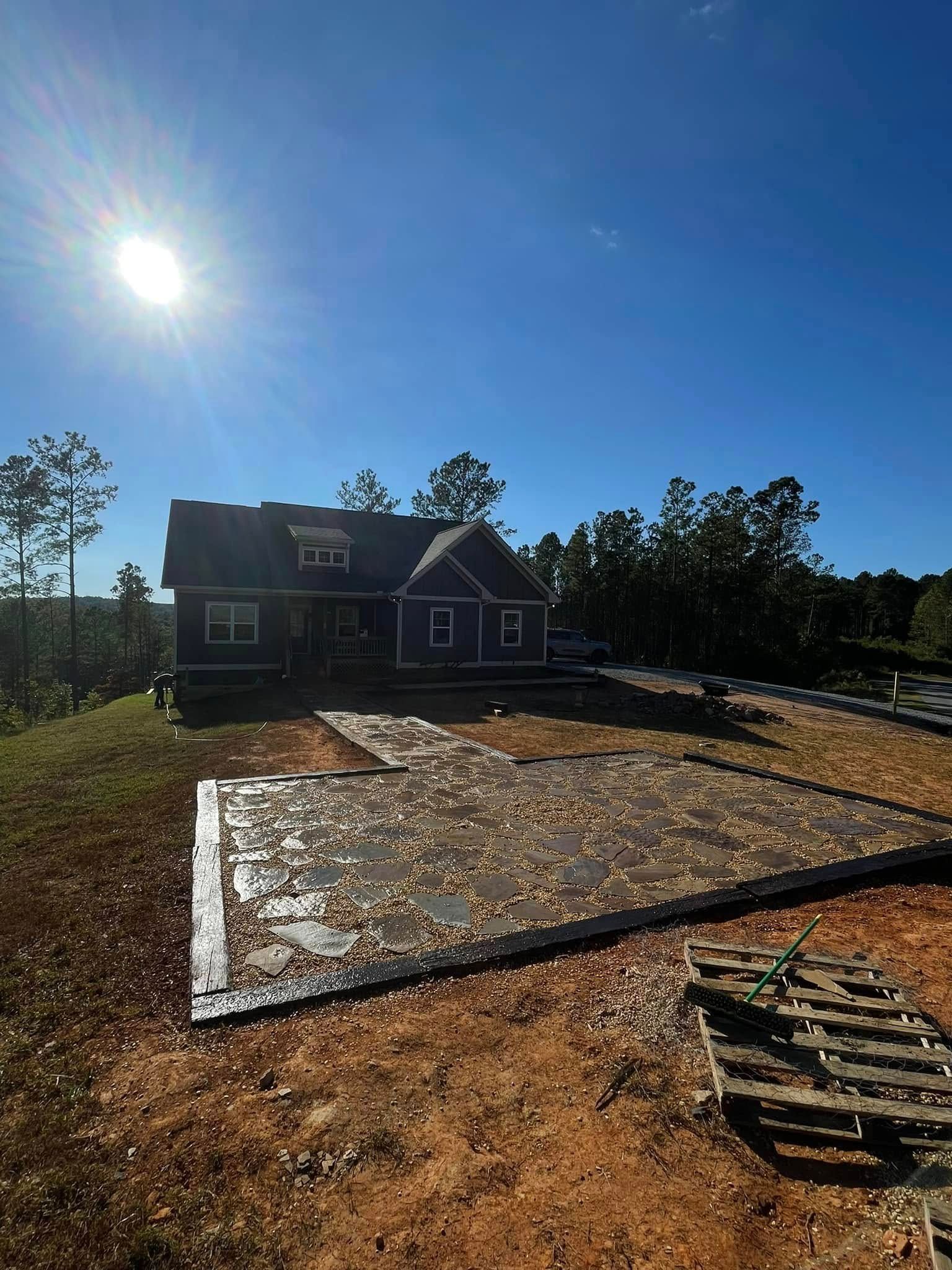 A dark blue house stands on a grassy lot under a bright, sunny sky, featuring a stone patio in the foreground.
