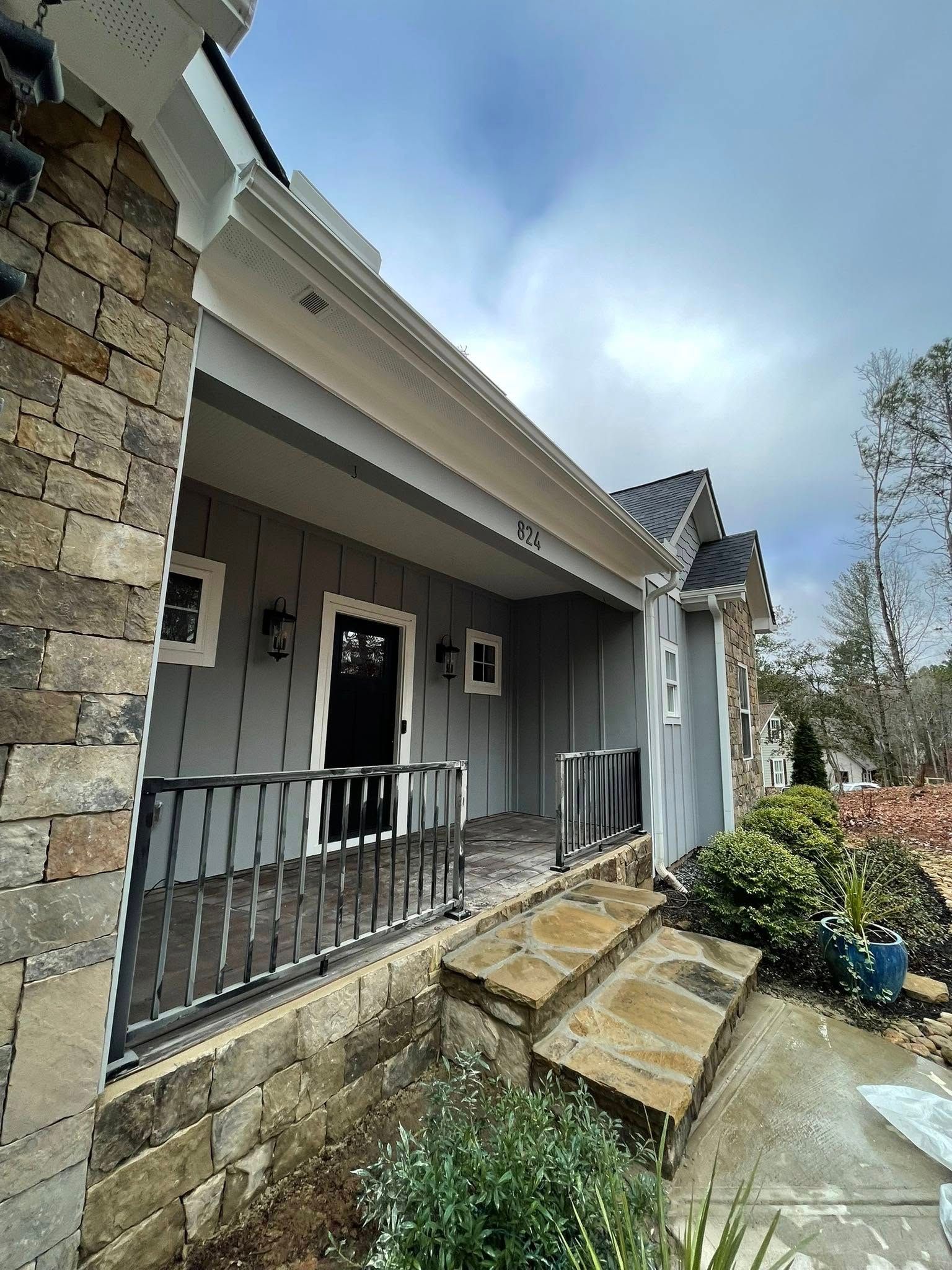 A front porch with grey board-and-batten siding, a black door, stone accents, and a metal railing.