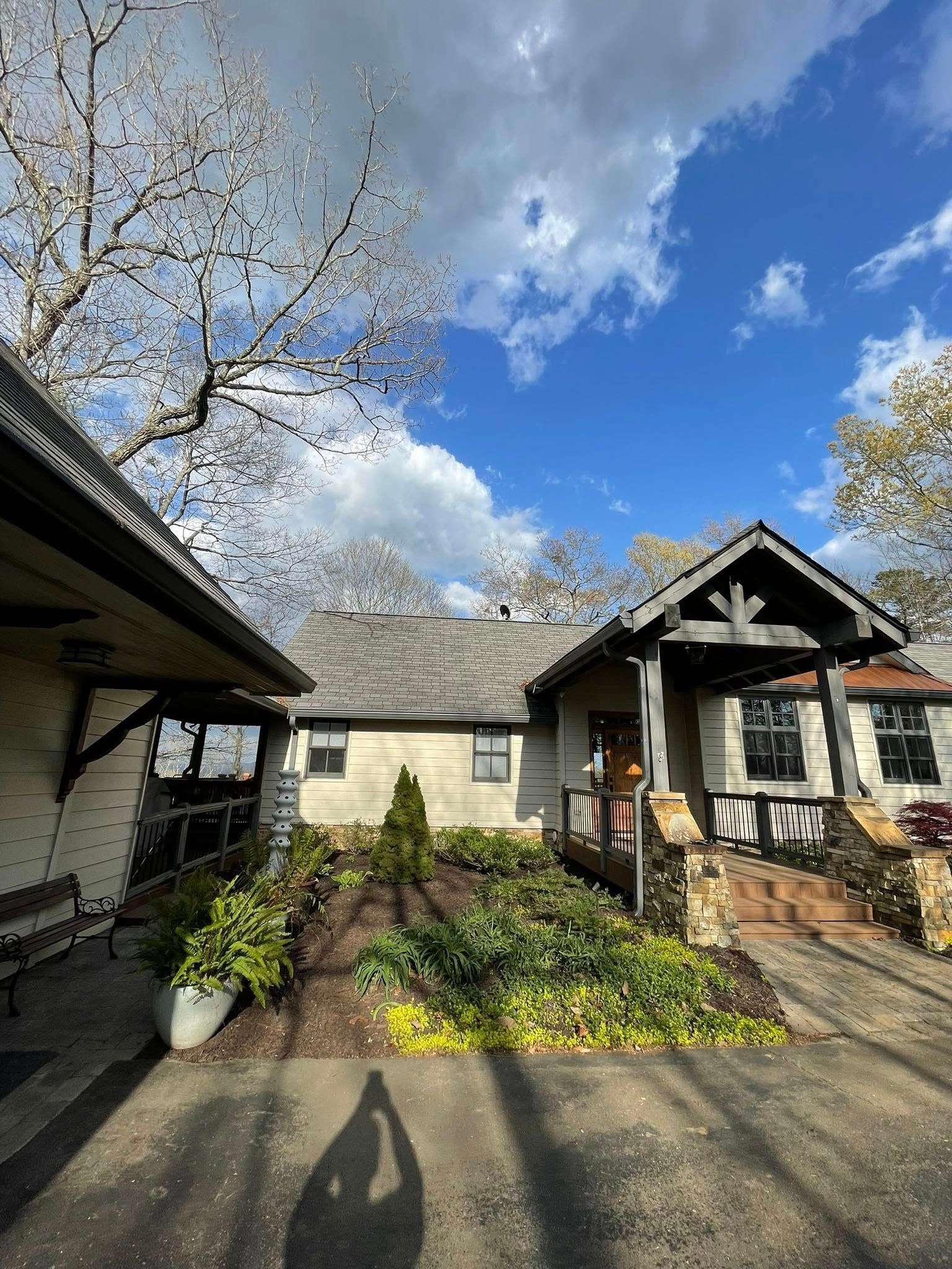 A single-story, light-colored building with a stone-accented porch under a cloudy blue sky, featuring front landscaping.