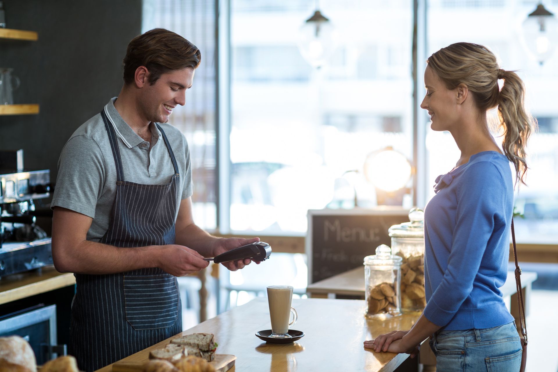 Barista serving a coffee to a smiling customer at a café counter