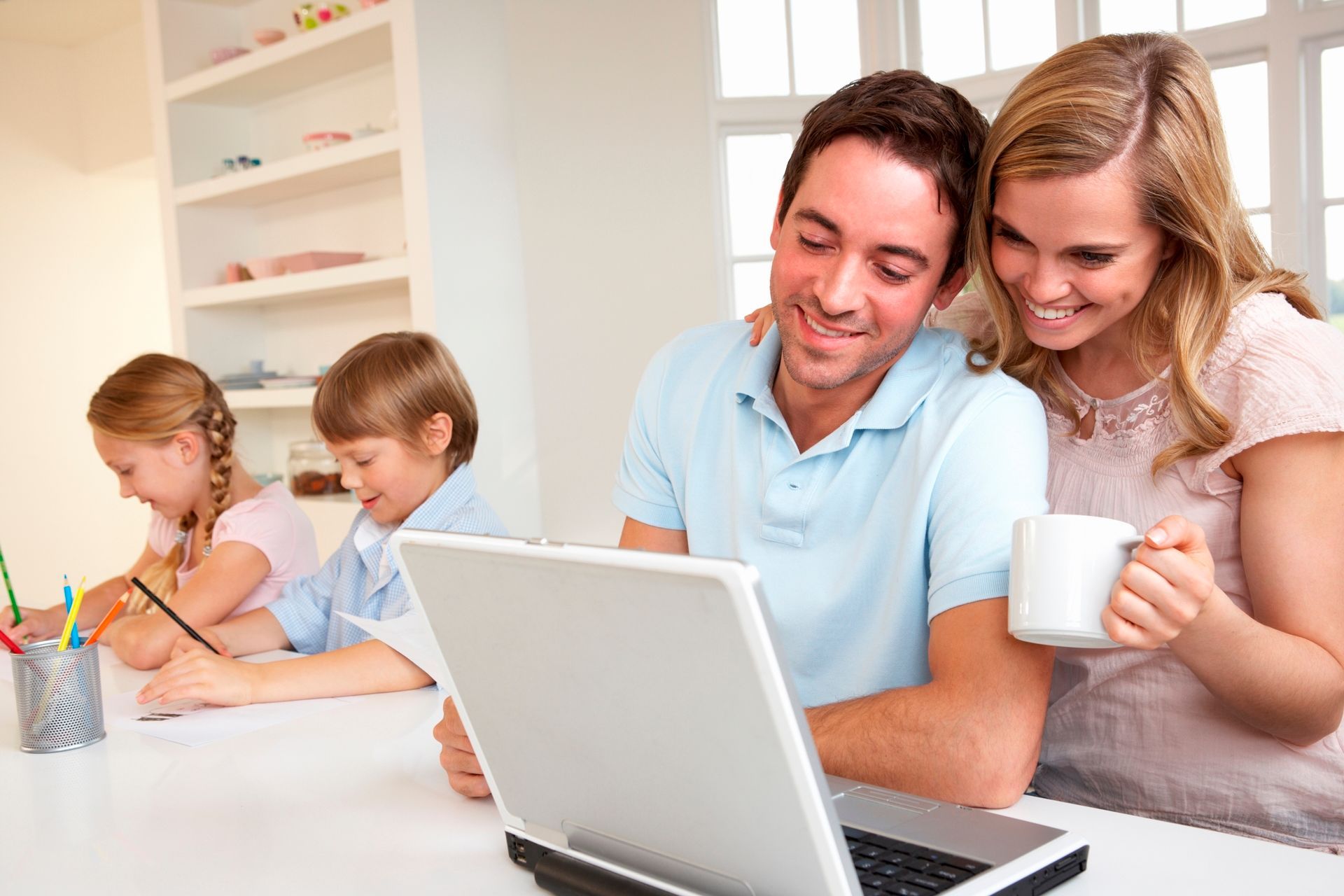 Family gathered around a laptop at a kitchen table, smiling and working together
